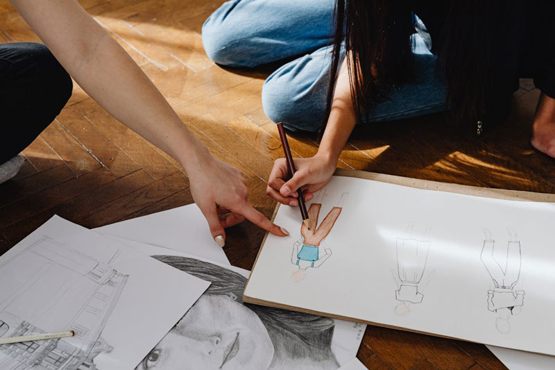 Une personne montre quelque chose à une autre personne qui dessine des bonhommes lors d’un atelier artistique